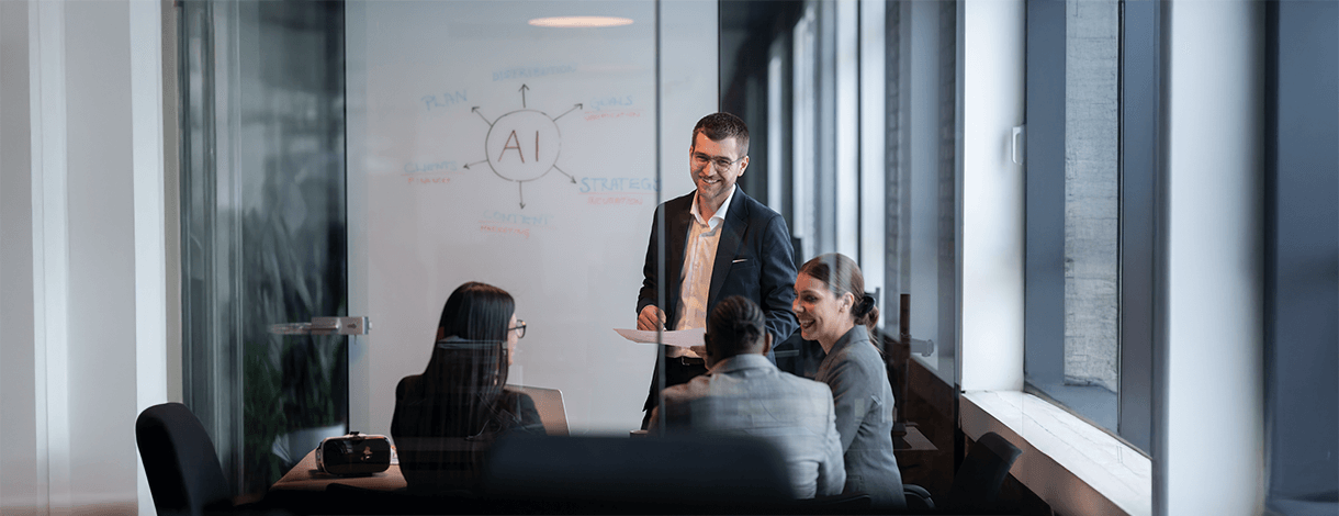 Vier Personen sitzen am Tisch und diskutieren über Künstliche Intelligenz (AI steht auf einem Whiteboard hinter ihnen)